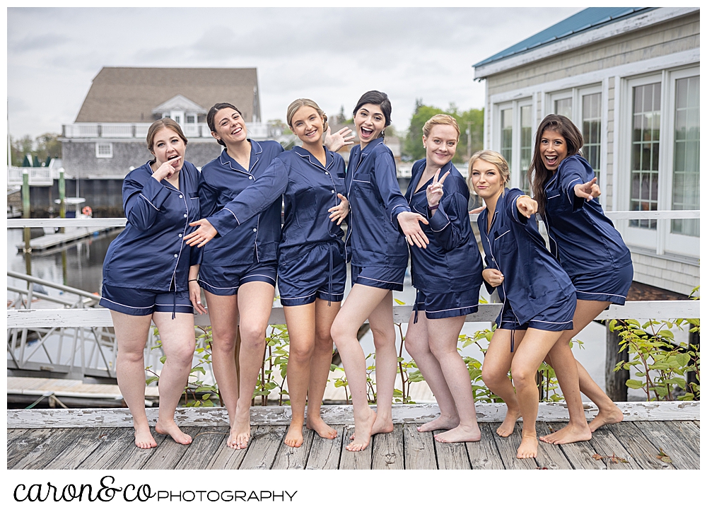 bridesmaids, dressed in short blue satin robes, smile for the camera on the dock in Kennebunkport Maine