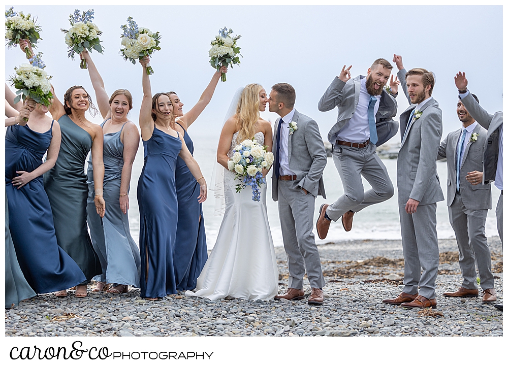a bride and groom kiss, while their wedding party cheers, and jumps!, for joy, at Colony Beach, Kennebunkport, Maine
