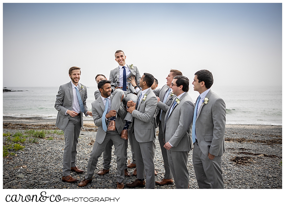 a group of groomsmen hoists the groom aloft as they have fun on Colony Beach Kennebunkport Maine
