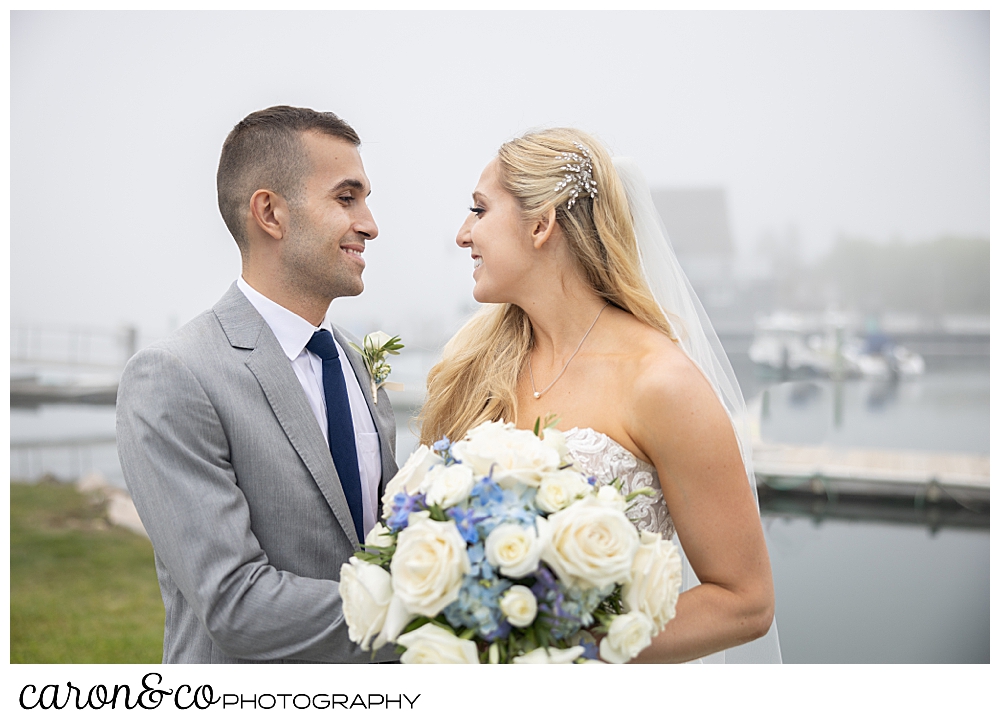 a bride and groom stand on a dock, smiling at one another, during their breakwater inn Kennebunkport wedding
