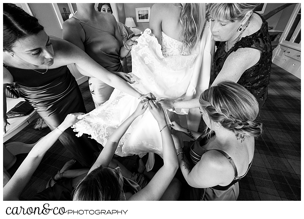 a black and white photo of bridesmaids helping to bustle the bride's dress at a breakwater inn Kennebunkport wedding reception
