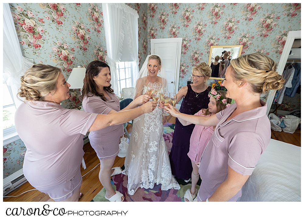 a bride, her bridesmaids, mother, and flower girl, toast with champagne flutes