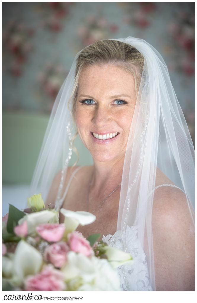 a beautiful bridal portrait of a smiling bride, her veil is over her shoulders, and a bridal bouquet is in front of the bride