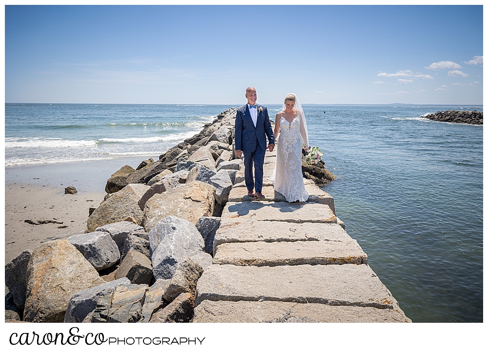 a bride and groom walk hand in hand on the Kennebunkport Maine breakwater