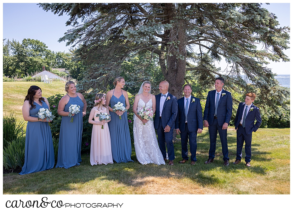 a bride and groom stand with their bridal party talking and laughing