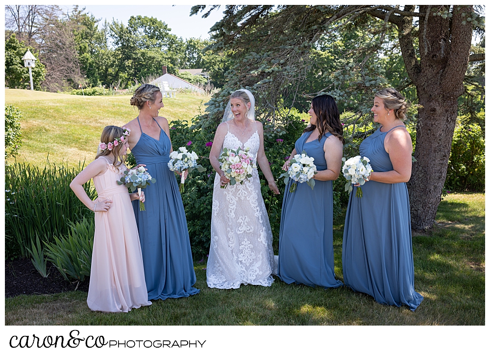 a bride and her bridesmaids stand together talking and laughing