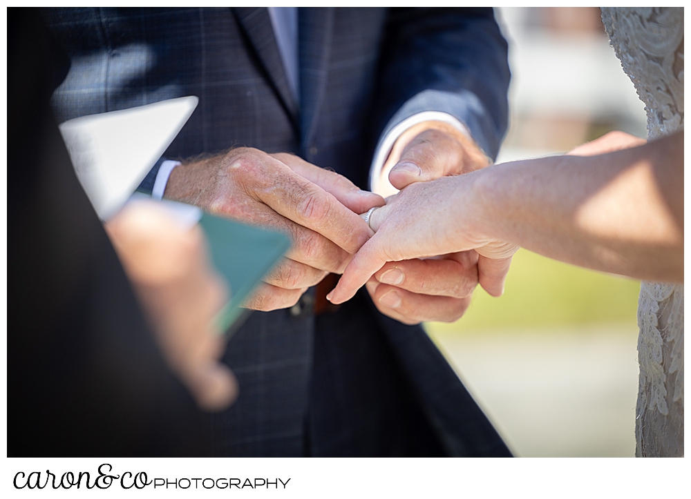 a groom's hands hold his bride's hand during the wedding ring ceremony during their Kennebunkport Maine colony hotel wedding