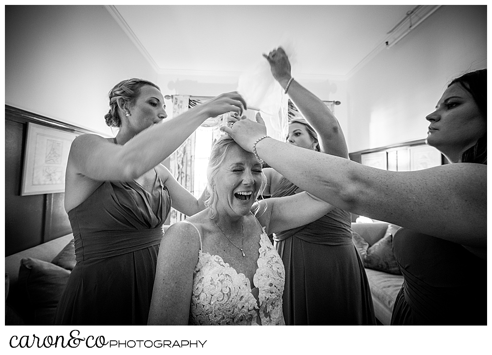 black and white photo of bridesmaids trying to remove a bride's veil as she laughs