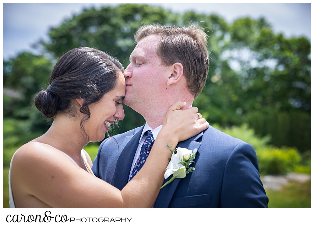 a groom kisses his bride on the forehead during their wedding day first look a their Kennebunkport Maine wedding at the colony hotel