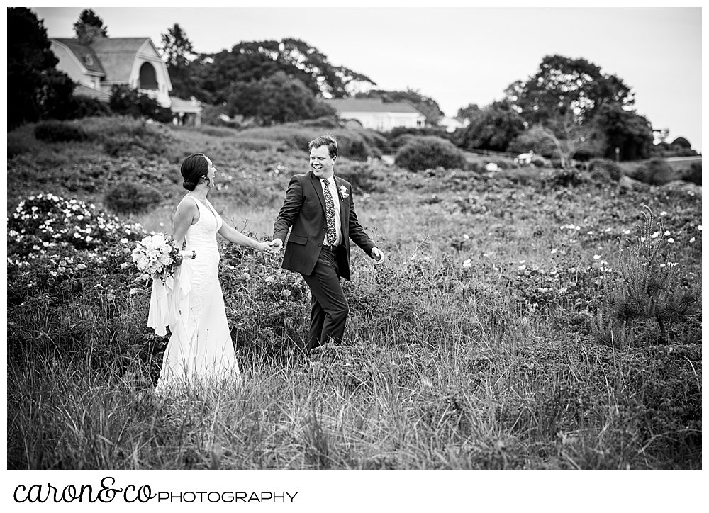 black and white photo of a bride and groom walking through the dunes, to Colony Beach in Kennebunkport Maine