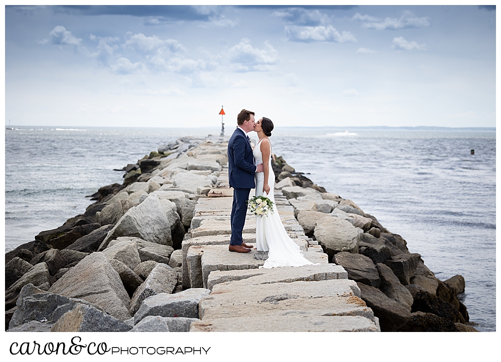a bride and groom kiss on top of the Kennebunkport Maine breakwater at Colony Beach