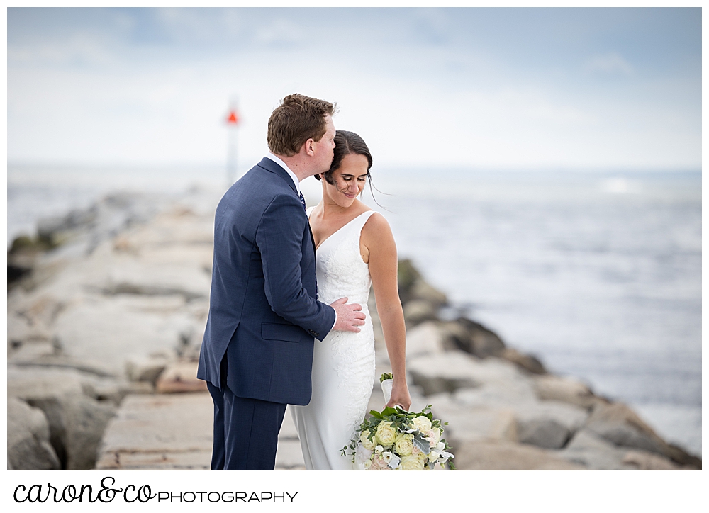 a bride kisses the brides forehead, while she has her eyes closed, they're standing on the Kennebunkport Maine breakwater at Colony beach