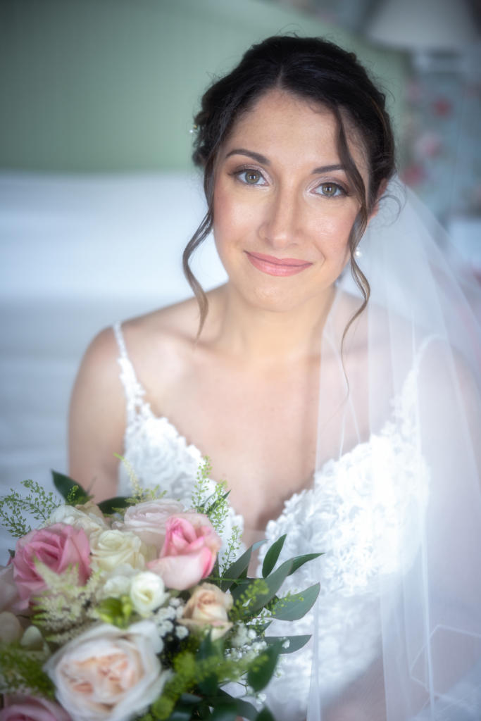a beautiful bridal portrait of a dark-haired bride, wearing a white dress and veil, holding a bouquet of pink, white, and green