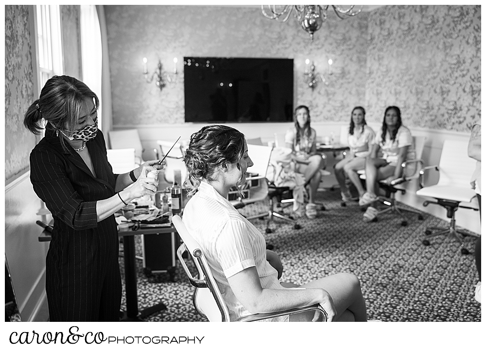a black and white photo of a bride having her hair done, while three of her bridesmaids look on