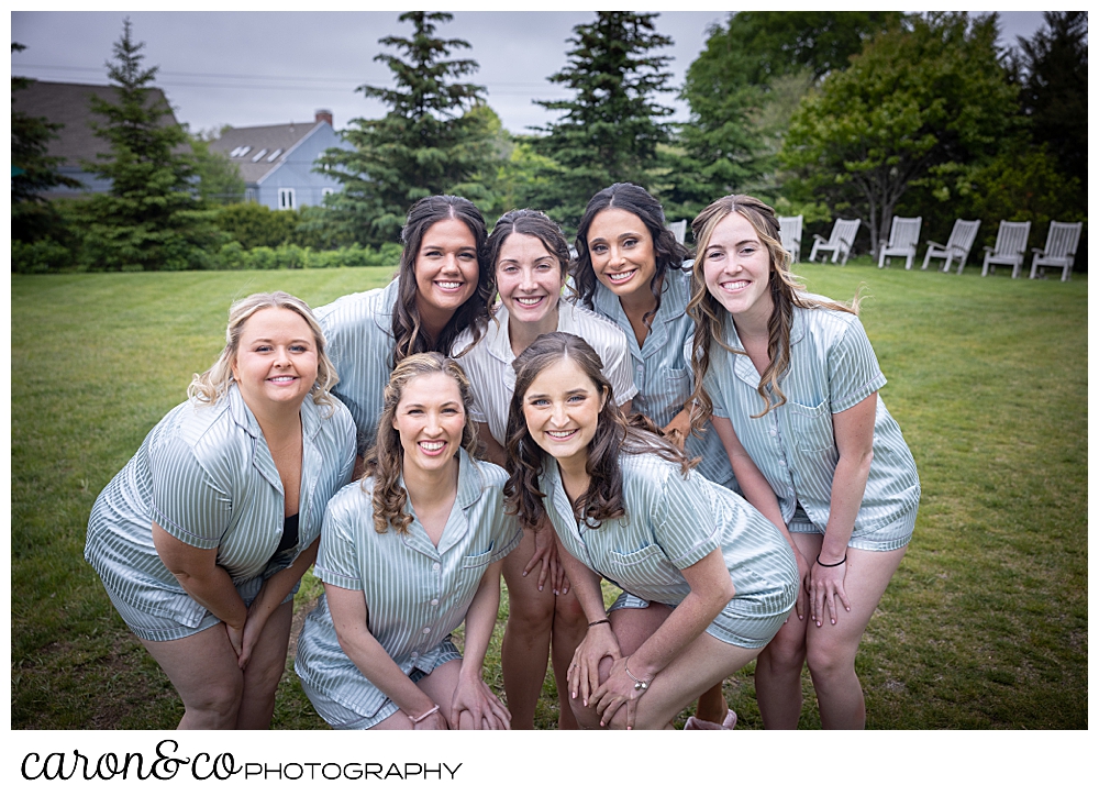 a bride in white pajamas is surrounded by her bridesmaids in light blue pajamas, they're all smiles