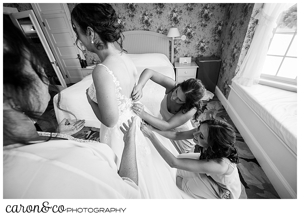 black and white photo of a bride getting into her dress, and her bridesmaids and mother are helping with the buttons in the back