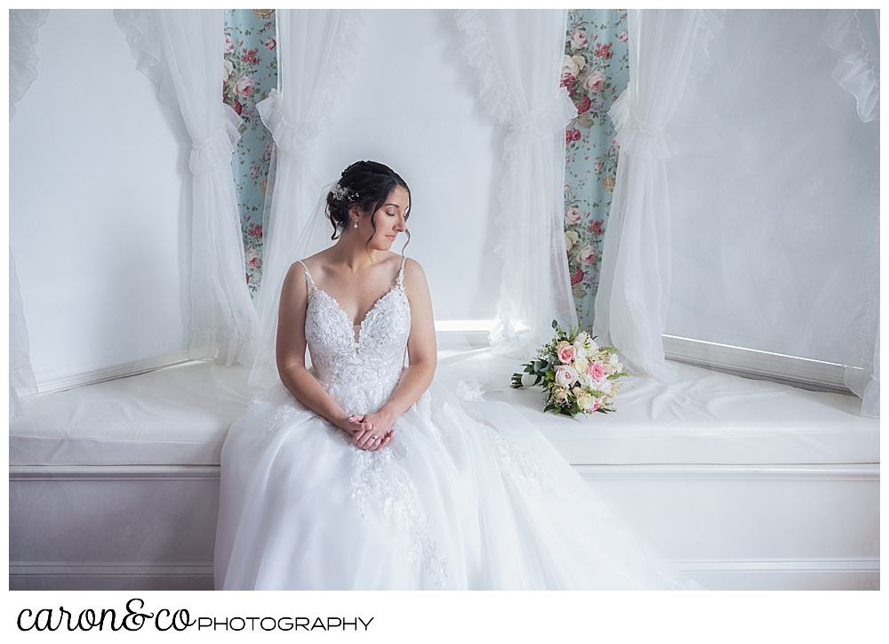 a beautiful bride sits in a window seat, her pastel bouquet is beside her
