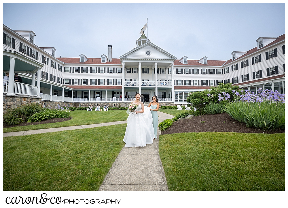a bride walking down a path at the Colony Hotel in Kennebunkport Maine, a bridesmaid is carrying her train