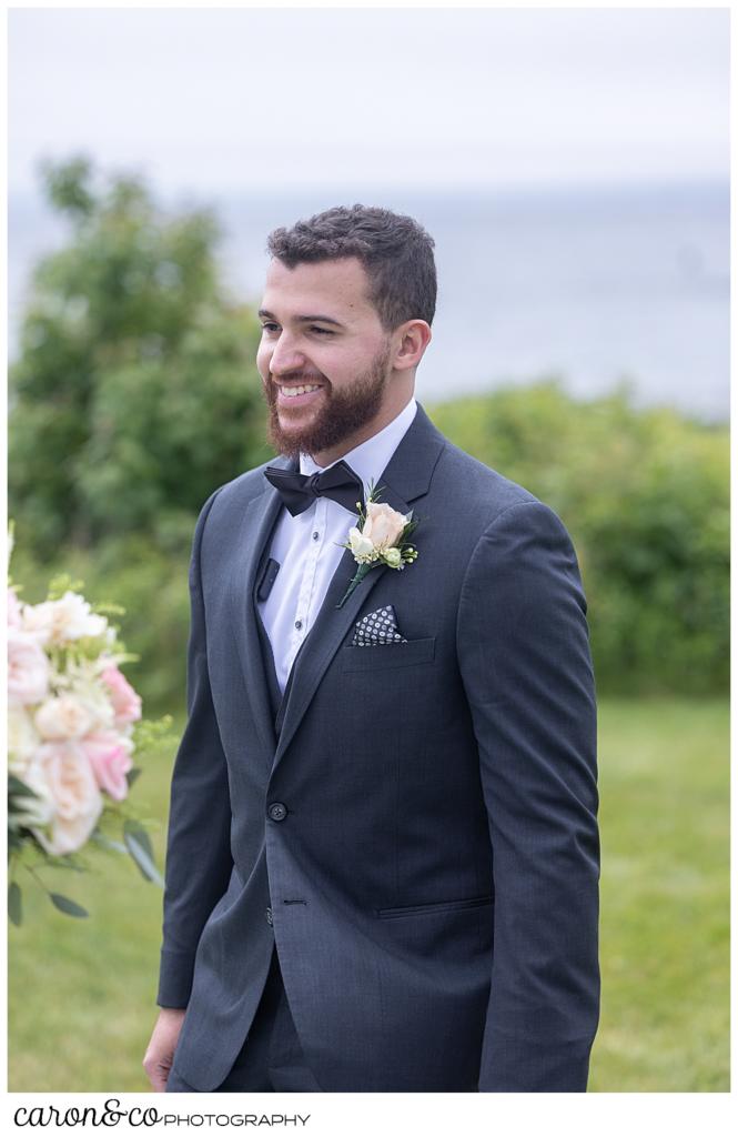 a groom in a gray suit, smiles during his wedding day first look