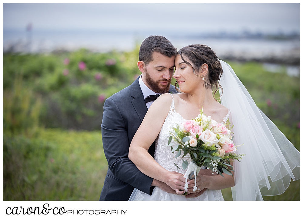 a bride and groom are standing back to front, their faces together, in a moment of solitude during their spring wedding at the colony hotel Kennebunkport maine
