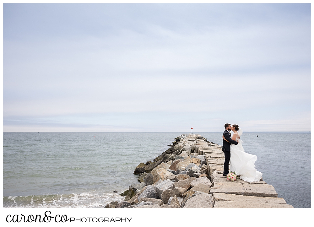a bride and groom are standing together, kissing, on top of the Kennebunkport Maine breakwater, in the foggy weather