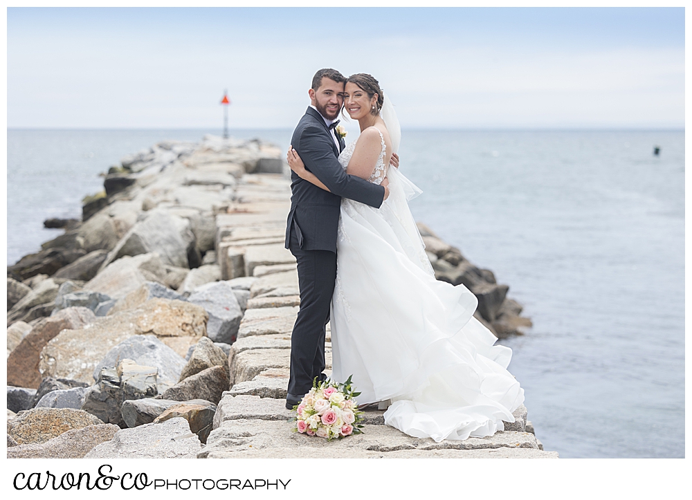 a bride and groom standing together, smiling, on top of the Kennebunkport Maine breakwater
