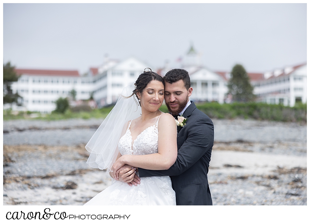 a bride and groom snuggle together, back to front, with the Colony Hotel, Kennebunkport, Maine