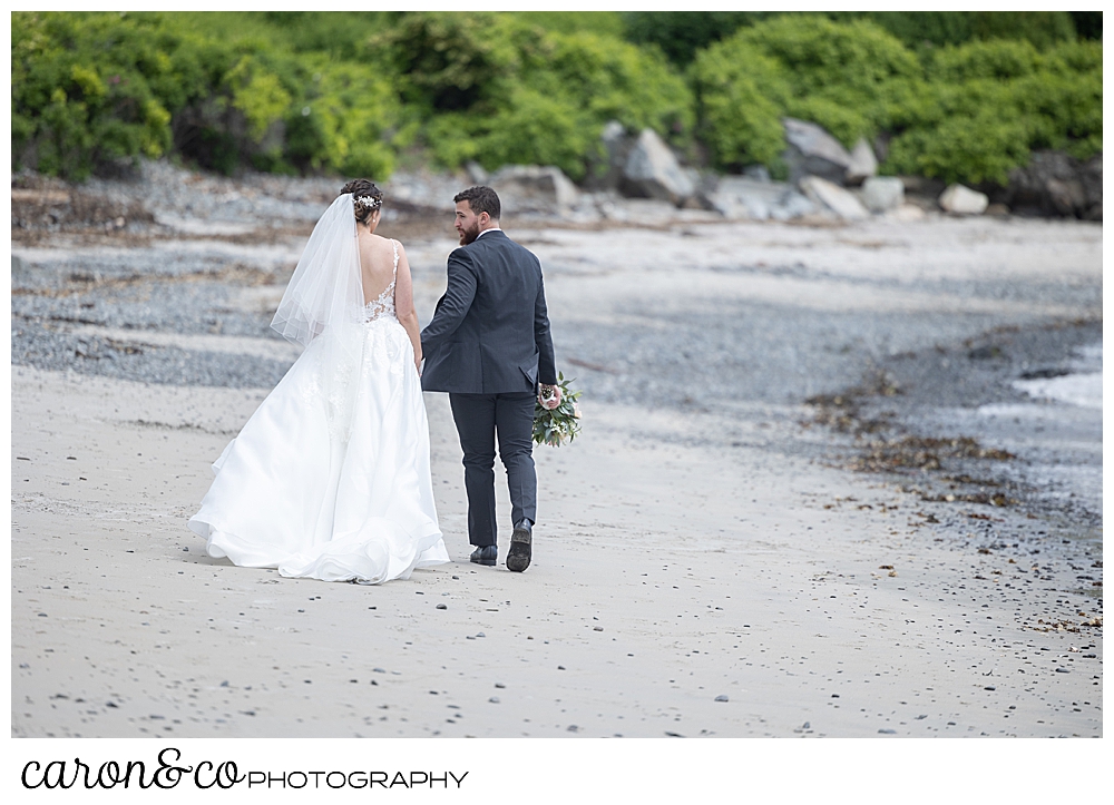 a bride and groom are walking hand in hand, away from the camera, so only their backs are visible on Colony Beach, Kennebunkport, Maine