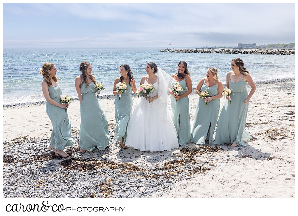 a bride is standing with her bridesmaids, dresses in sage green, on Colony Beach, Kennebunkport, Maine