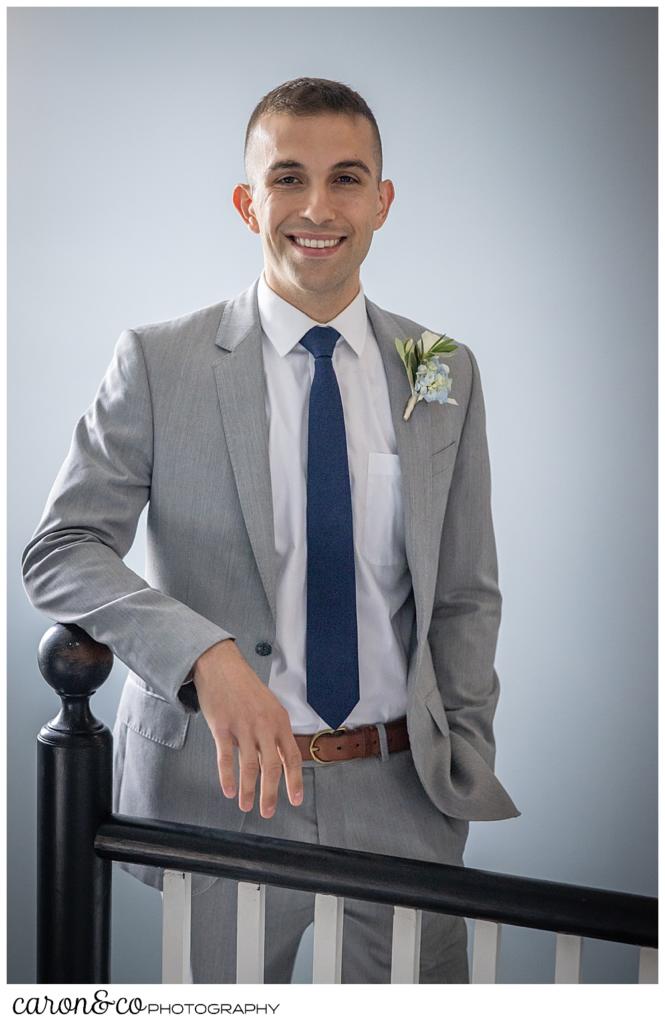 a groom in a gray suit, poses in a stairway