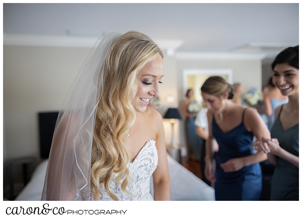 a bride smiles as her bridesmaids help with her wedding dress