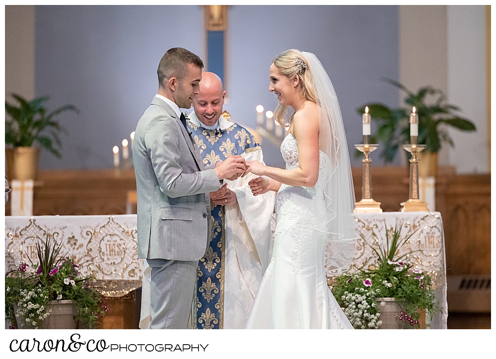 a bride and groom stand at the altar, during the ring exchange at St. Joseph's Church, Biddeford, Maine