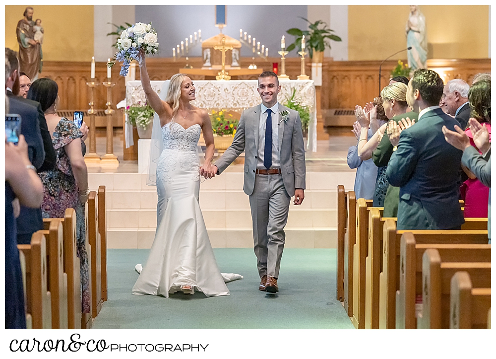 a smiling bride and groom during their recessional at St. Joseph's Church, Biddeford, Maine, the bride is holding her bridal bouquet above her head