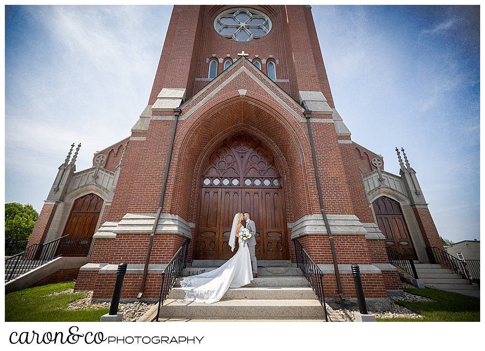 a bride and groom pose in front of st. Joseph's church Biddeford, Maine, on their wedding day