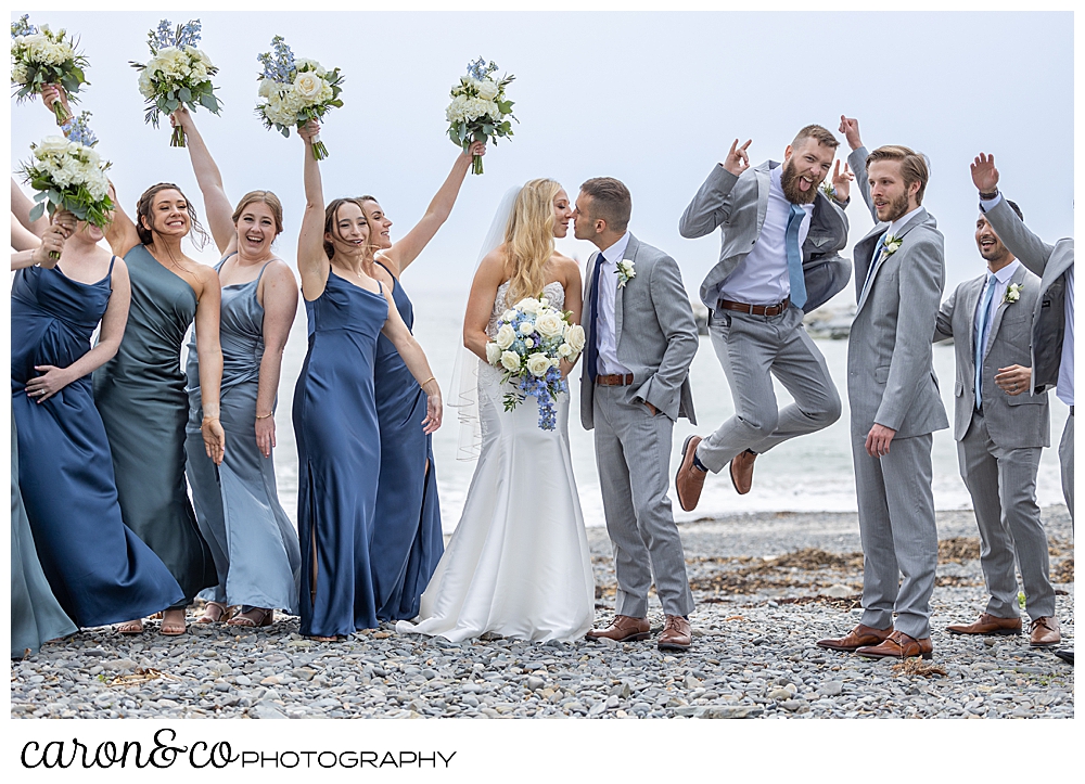 a bride and groom kiss, while their bridal party jumps and cheers