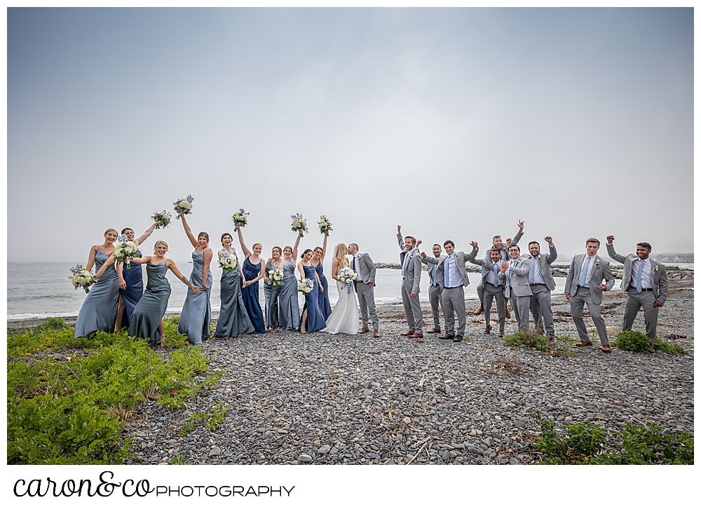 a bride and groom kiss while their bridal party cheers them on, at Colony Beach, Kennebunkport, Maine