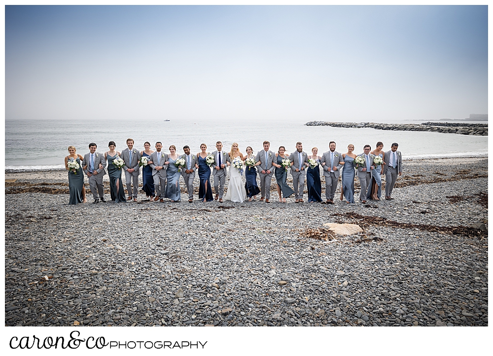 a bridal party of twenty one, has their arms linked as they walk up Colony Beach in Kennebunkport, Maine