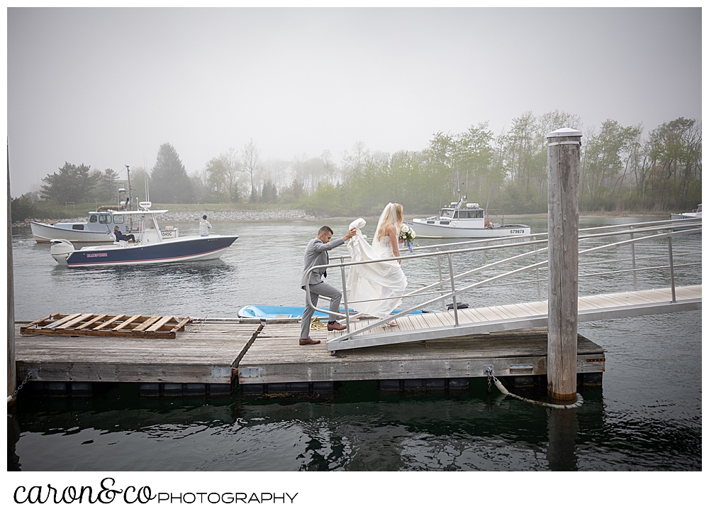 a bride walks up a dock ramp in foggy Kennebunkport, Maine, her groom is carrying her train as he follows behind